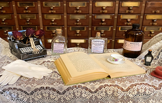 An opened book with a teacup atop it, surrounded by bottles and a typewriter.